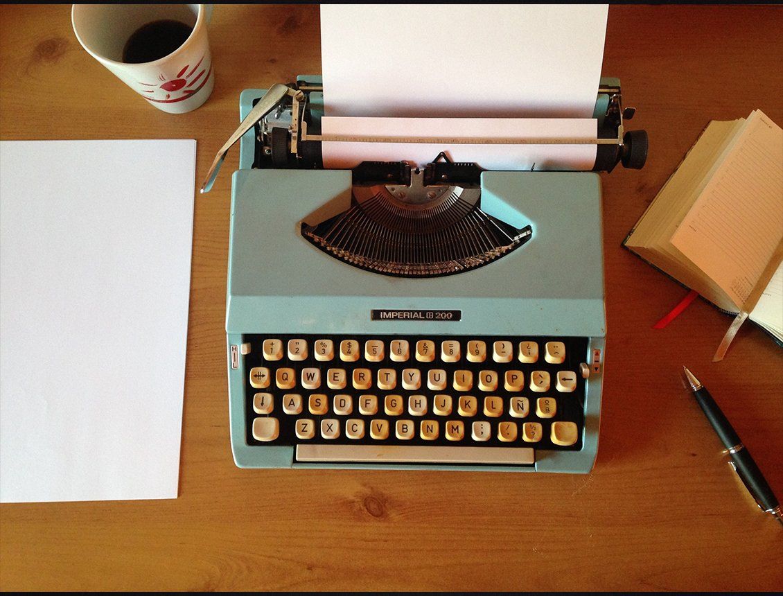 Top down image of an old style typewriter A typewriter is sitting on a wooden table next to a cup of coffee