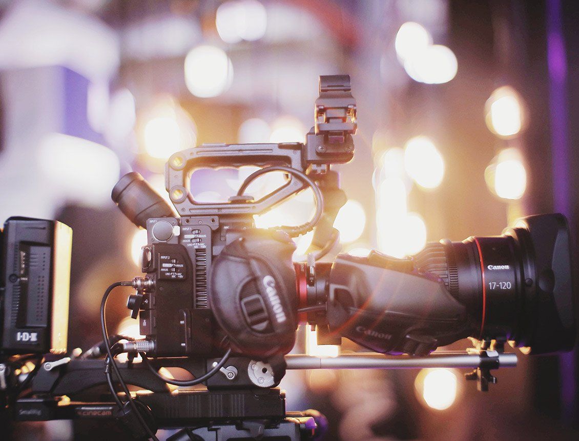 Close up Canon cinema camera with Canon zoom lens with bokeh lights in background A close up of a video camera sitting on top of a table.