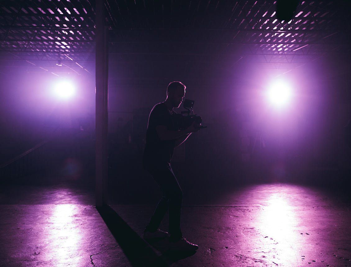 A man is standing in a dark room with purple lights.
