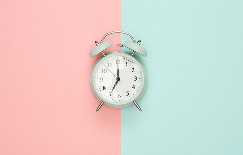 Image of an analog clock over pink and aqua color background Alarm clock on a pink and blue background, clock shows 7:00.
