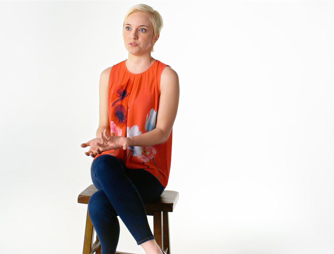 A woman is sitting on a wooden stool with her legs crossed.