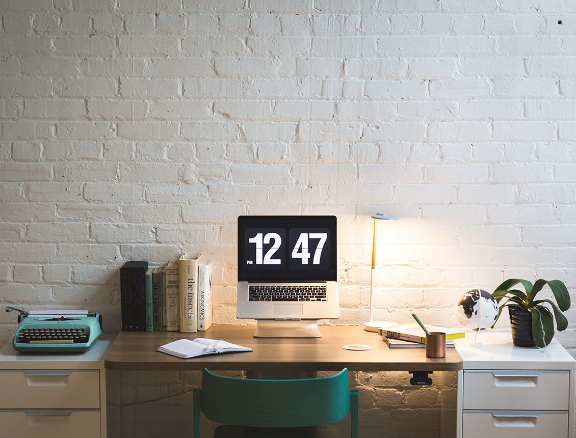 Image of a desk in front of a white brick wall with laptop that has 12:47pm on screen Image of a desk in front of a white brick wall with laptop that has 12:47pm on screen
