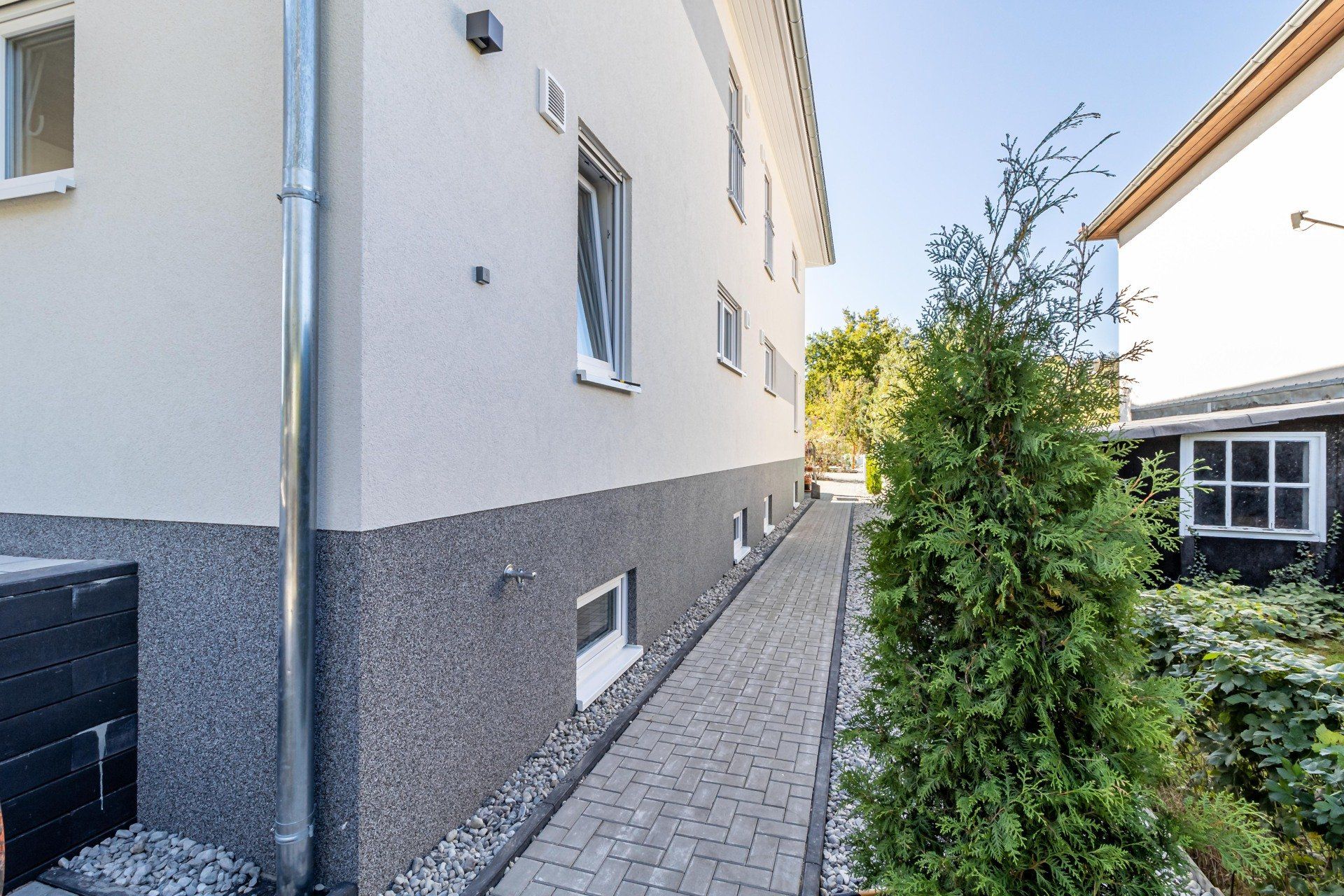 Ein Gehweg, der zu einem Haus führt, im Vordergrund steht ein Baum.