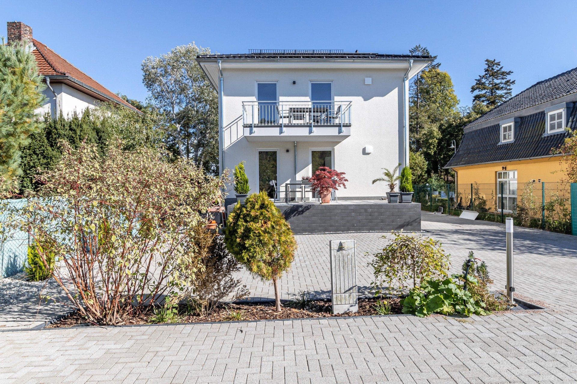 Ein weißes Haus mit Balkon ist von Bäumen und Büschen umgeben.