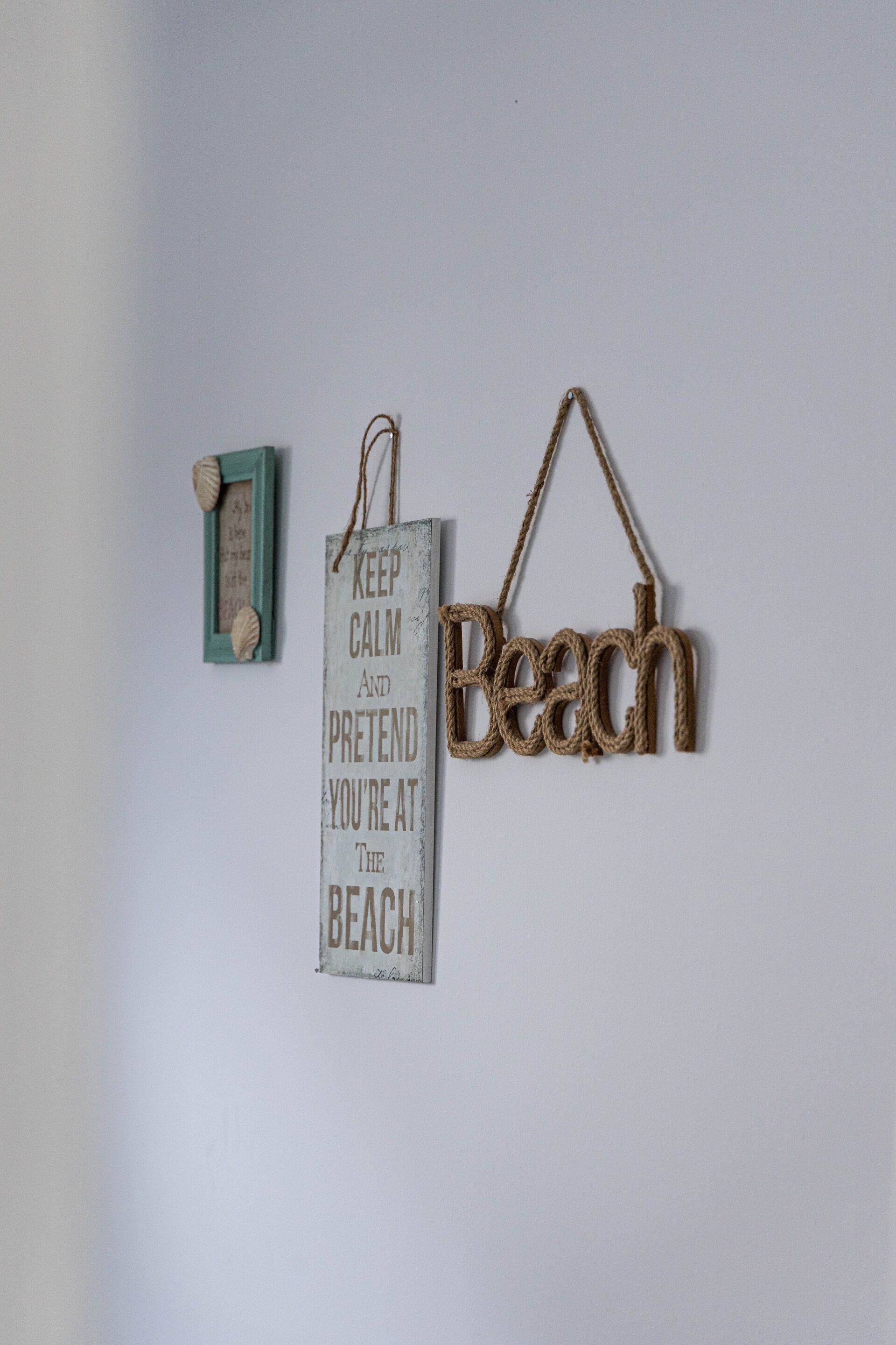Eine weiße Wand, an der ein Schild mit der Aufschrift „Strand“ hängt.