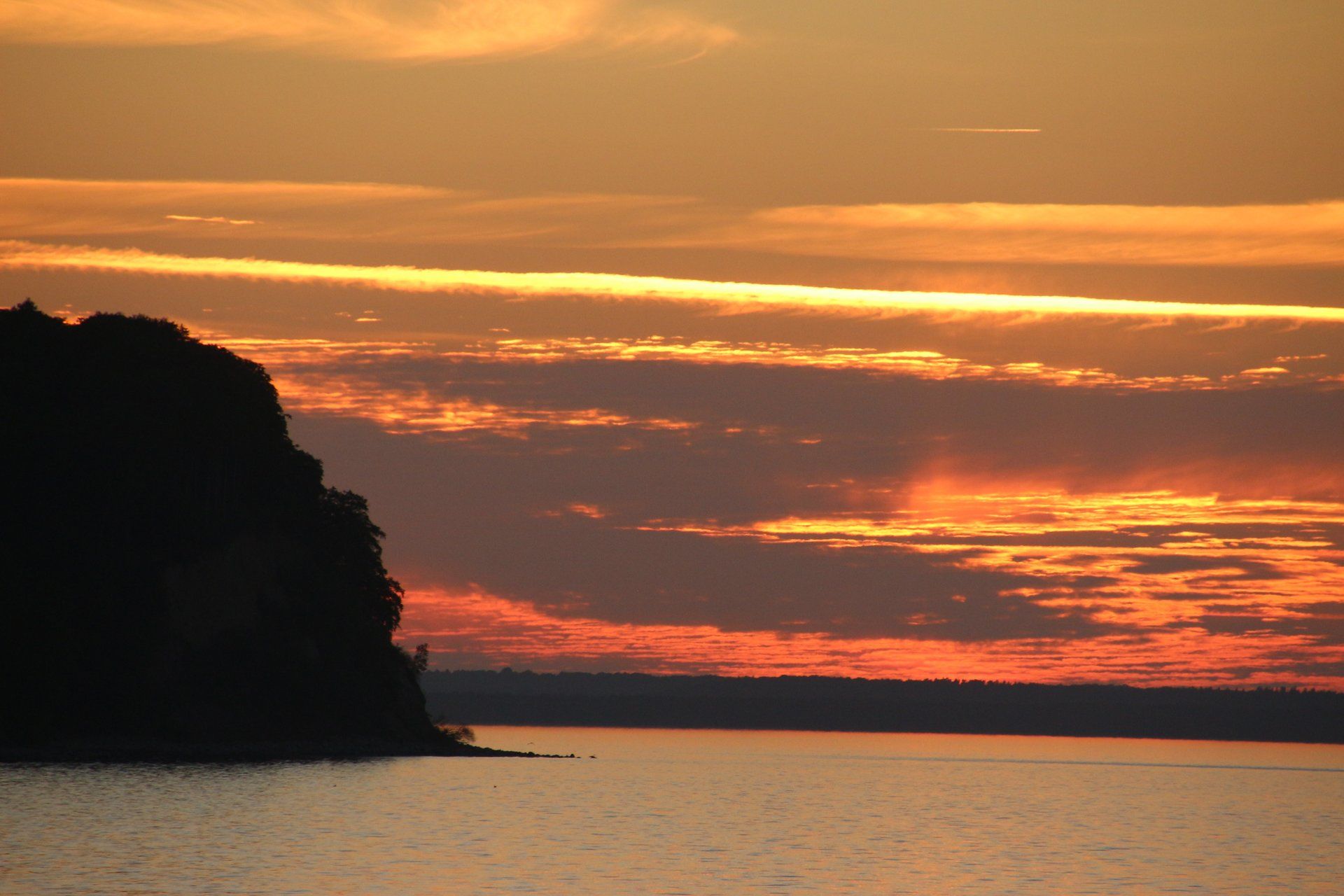 Ein Sonnenuntergang über einem Gewässer mit einem großen Felsen im Vordergrund