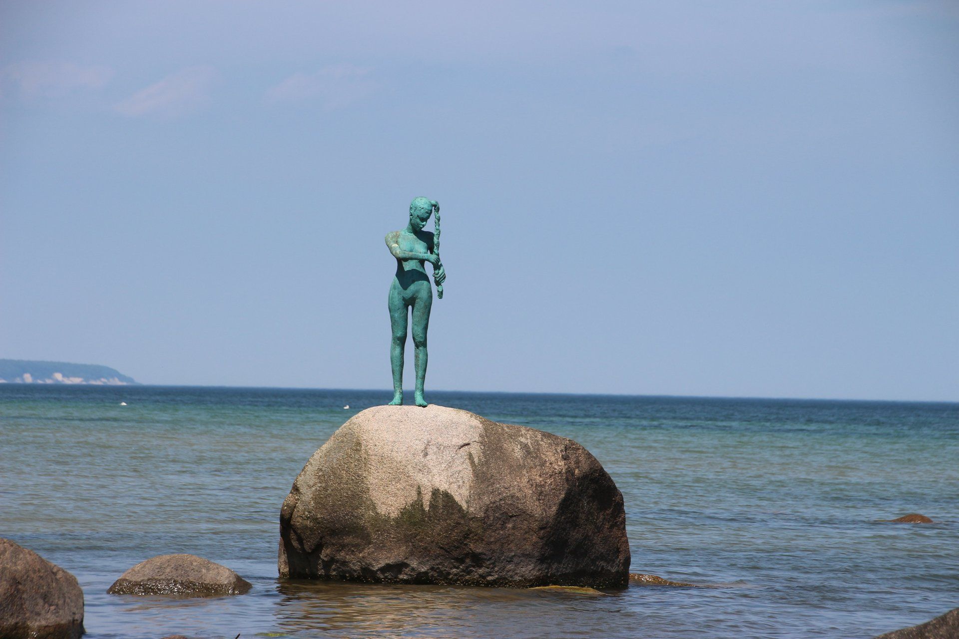 Eine Frauenstatue, die auf einem großen Felsen mitten im Ozean steht.