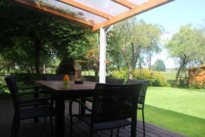 Eine Terrasse mit Tisch und Stühlen unter einem Baldachin mit Blick auf eine üppige grüne Wiese.