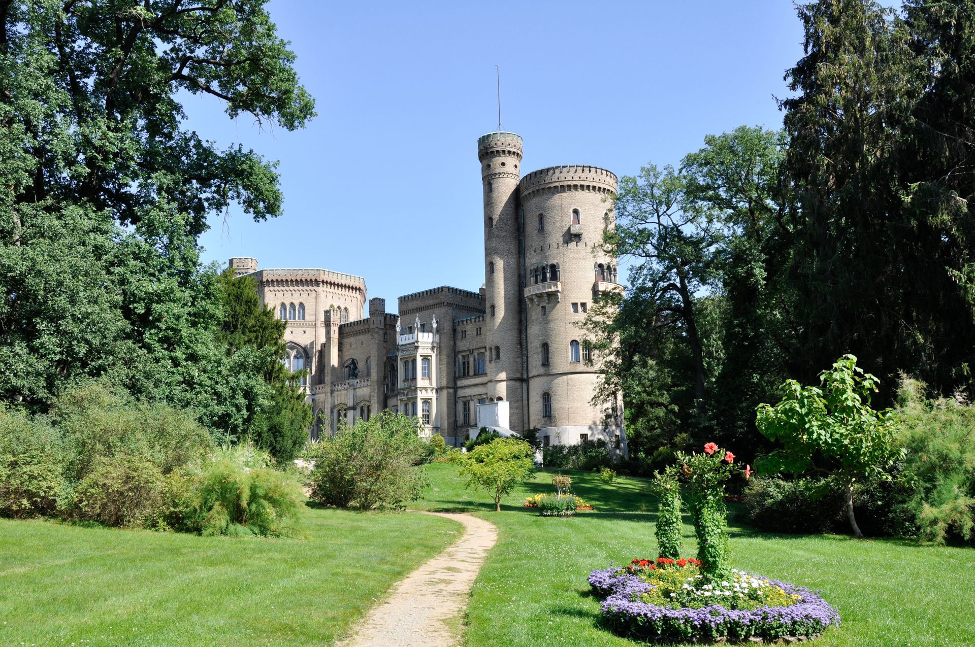 Ein Schloss ist von Bäumen und Blumen in einem Park umgeben.