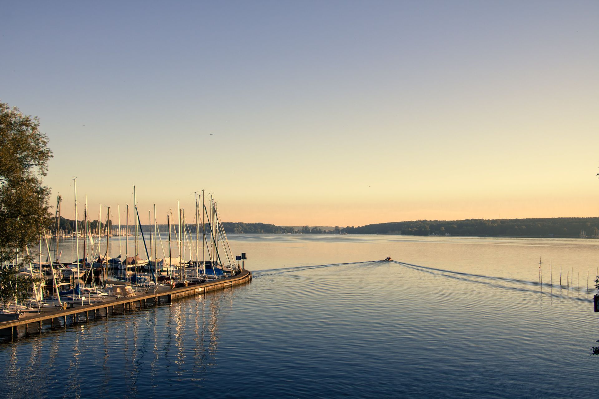 Eine große Wasserfläche mit Booten, die bei Sonnenuntergang am Ufer vor Anker liegen.