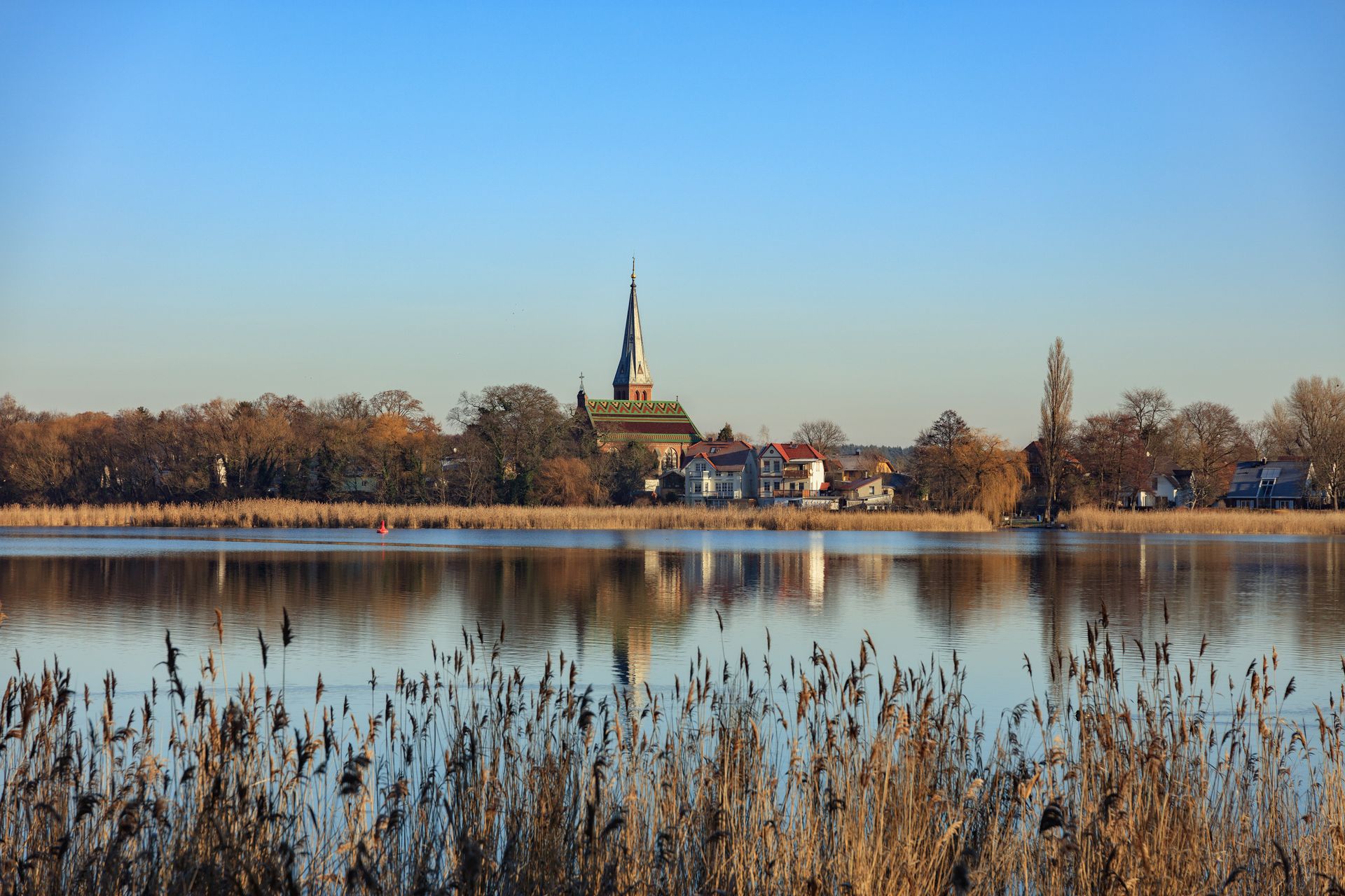 Ein See mit einer Kirche im Hintergrund und hohem Gras im Vordergrund