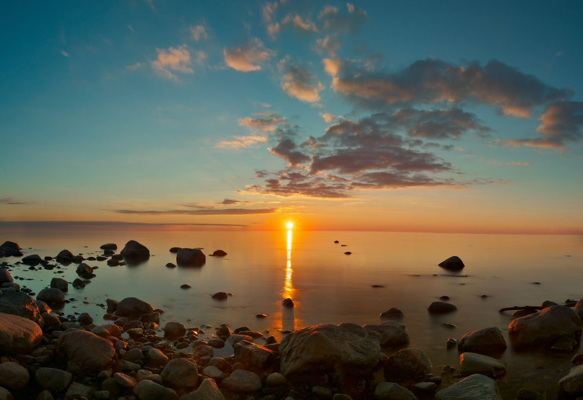 Die Sonne geht über dem Meer unter, im Vordergrund sind Felsen zu sehen.
