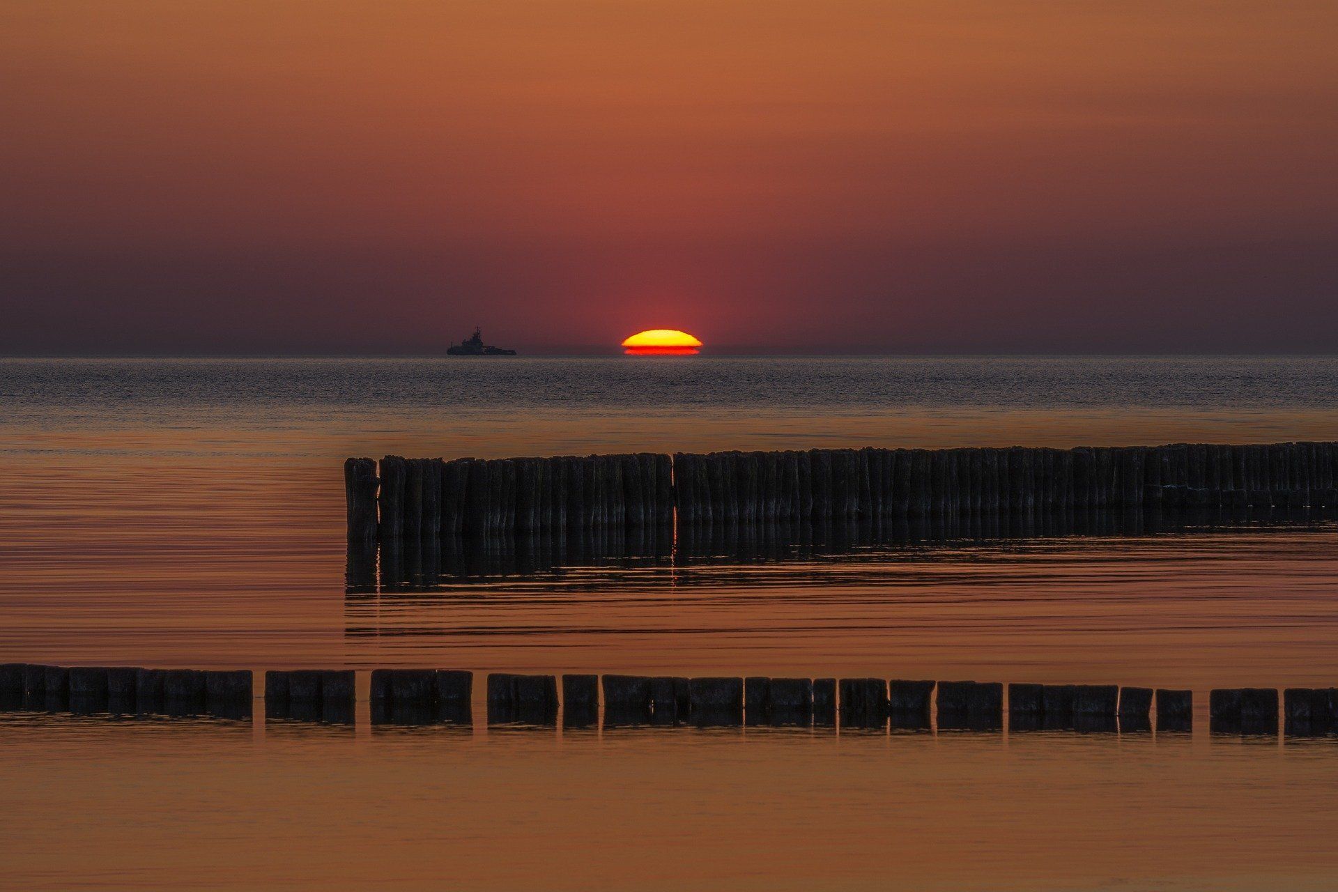 Die Sonne geht über dem Meer unter, in der Ferne ist ein Boot zu sehen.
