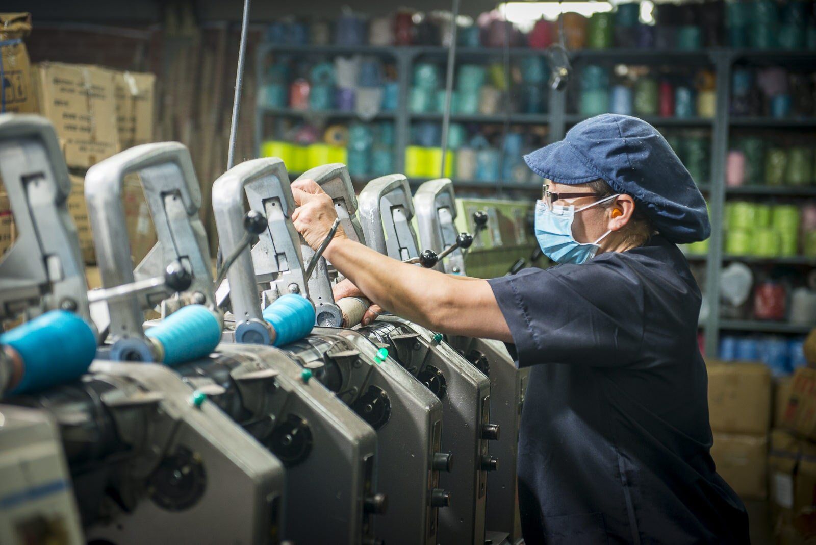 Worker wearing a mask operates industrial machinery in a factory workshop.