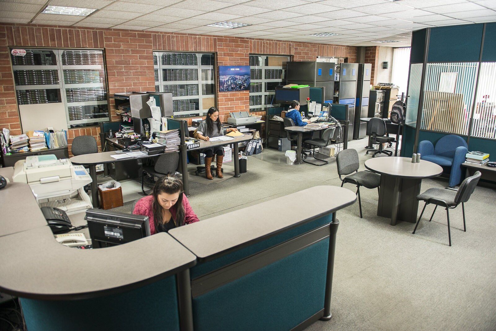 Open office reception area with desks, computers, and a few people working and sitting nearby