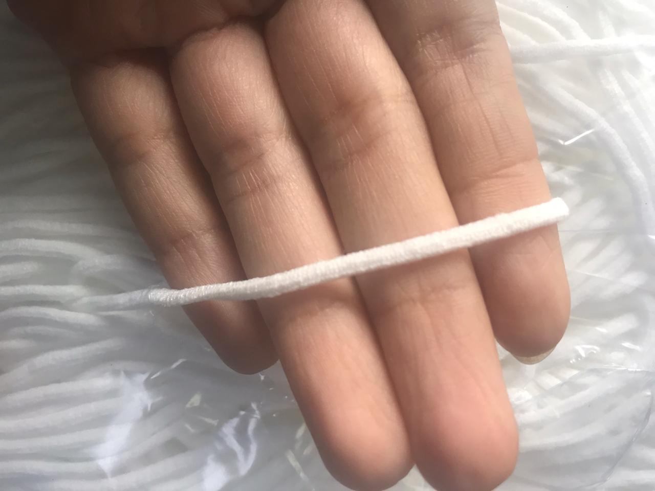 Close-up of a hand holding a white cord against a soft, white textured background
