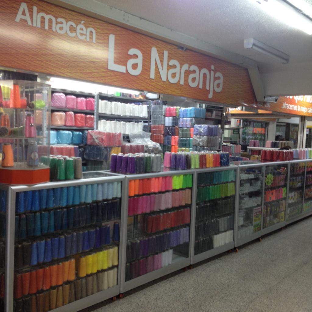 Colorful yarn and craft supplies displayed in a store aisle under a sign reading “Almacén La Naranja”