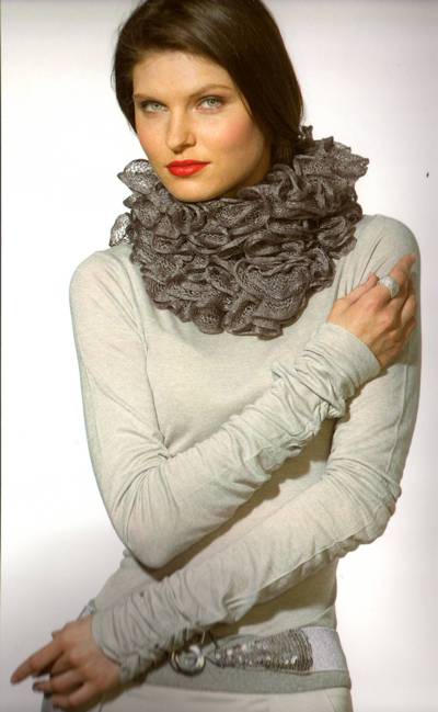 Woman in a light sweater with a ruffled gray scarf, standing with arms crossed against a plain background.