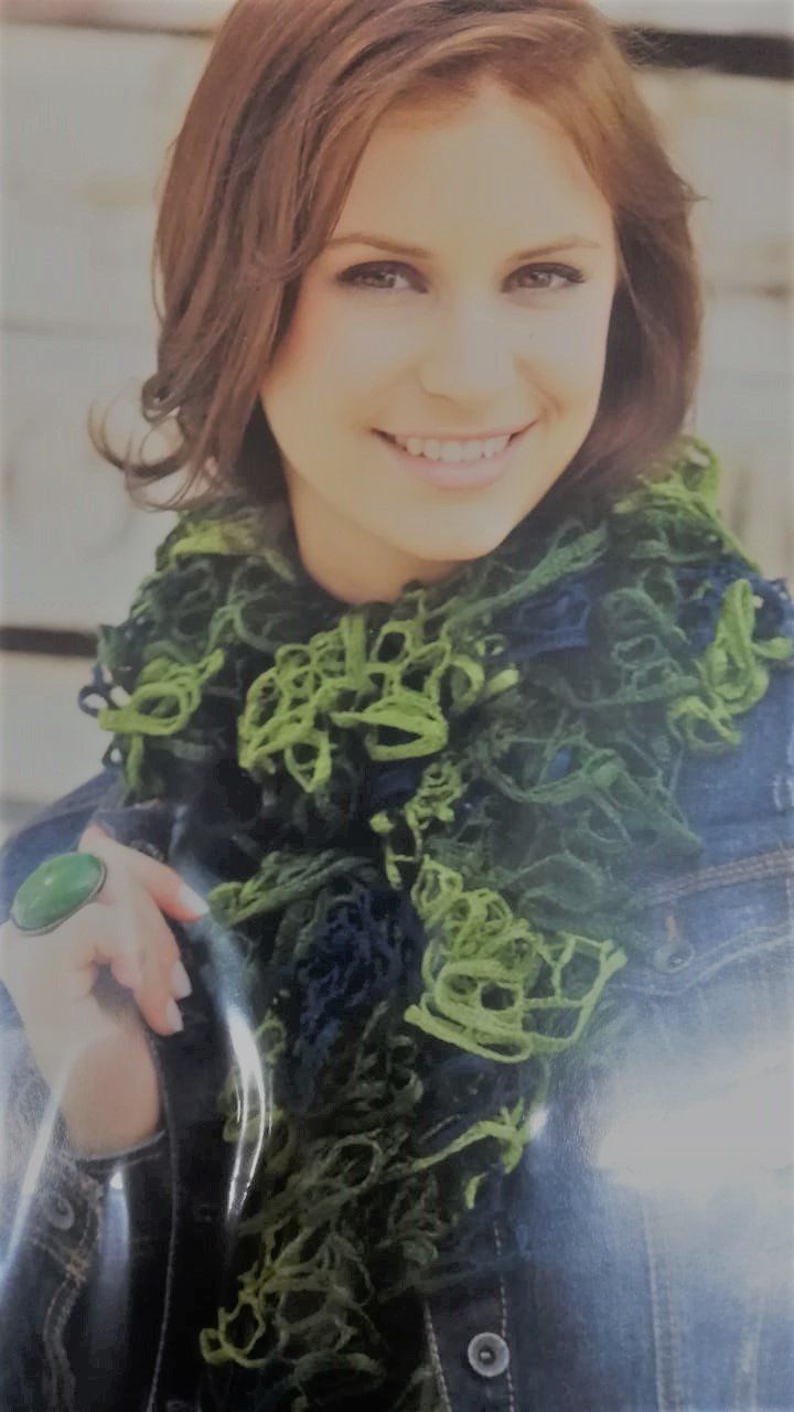 Smiling woman in a denim jacket and green scarf, holding a strap outdoors