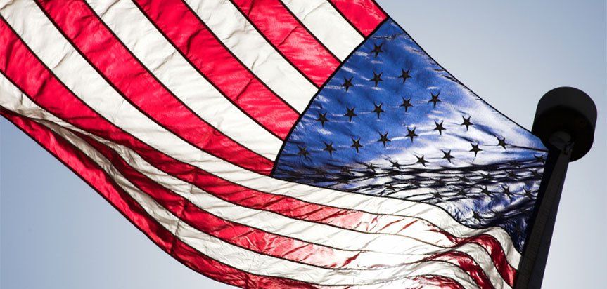 An american flag is waving in the wind against a blue sky.