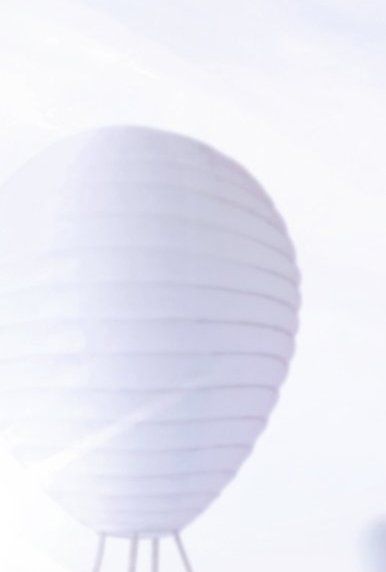 Weiße Papierlaterne in Kugelform auf einem Dreibeinsockel vor einem strahlend weißen Hintergrund.