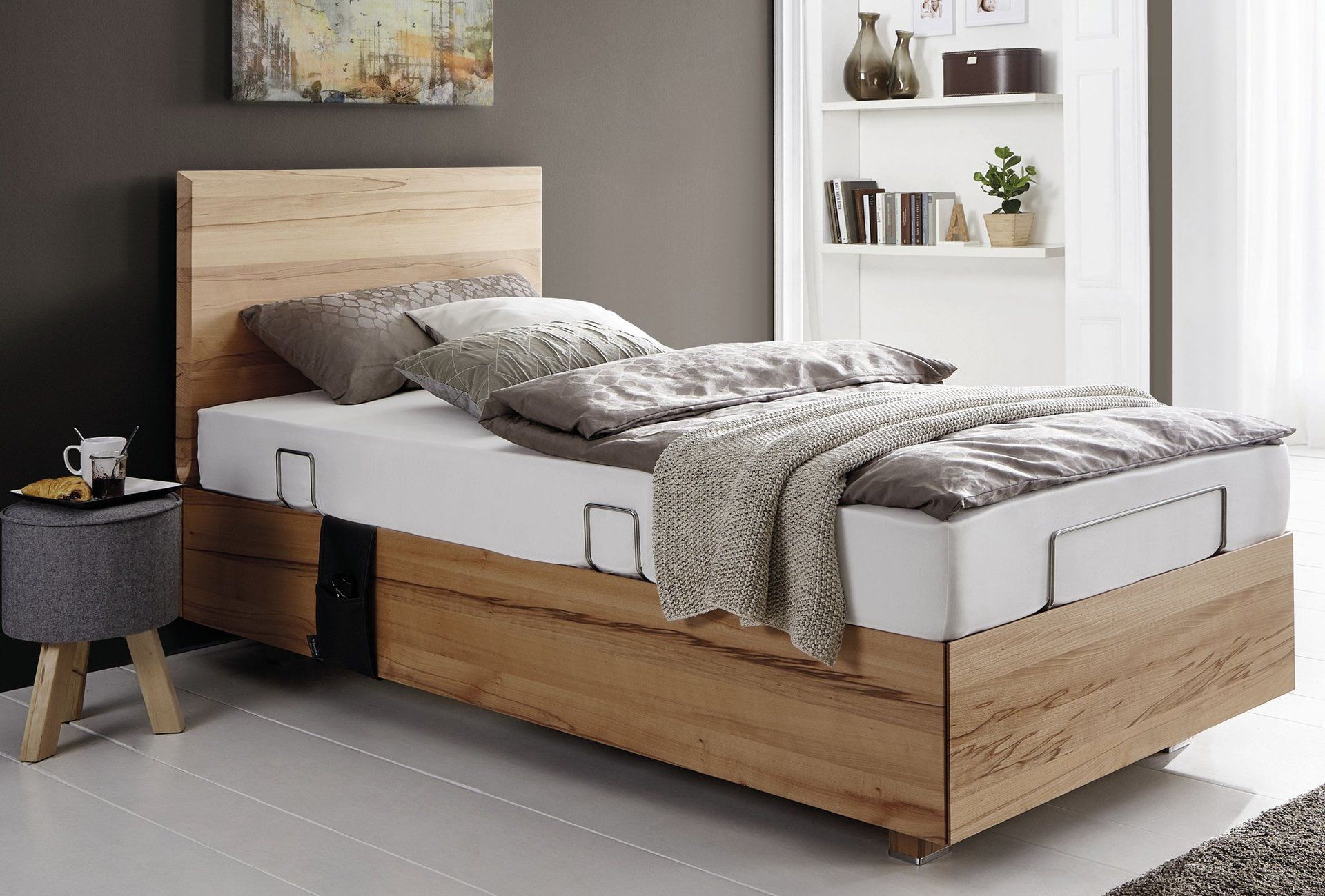Einzelbett aus Holz mit weißer Matratze und Bettbezug. Neben dem Bett steht ein Beistelltisch.