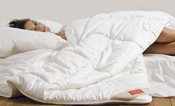 Frau im Bett, teilweise mit einer weißen Bettdecke bedeckt. Sie legt ihren Kopf auf ein Kissen.