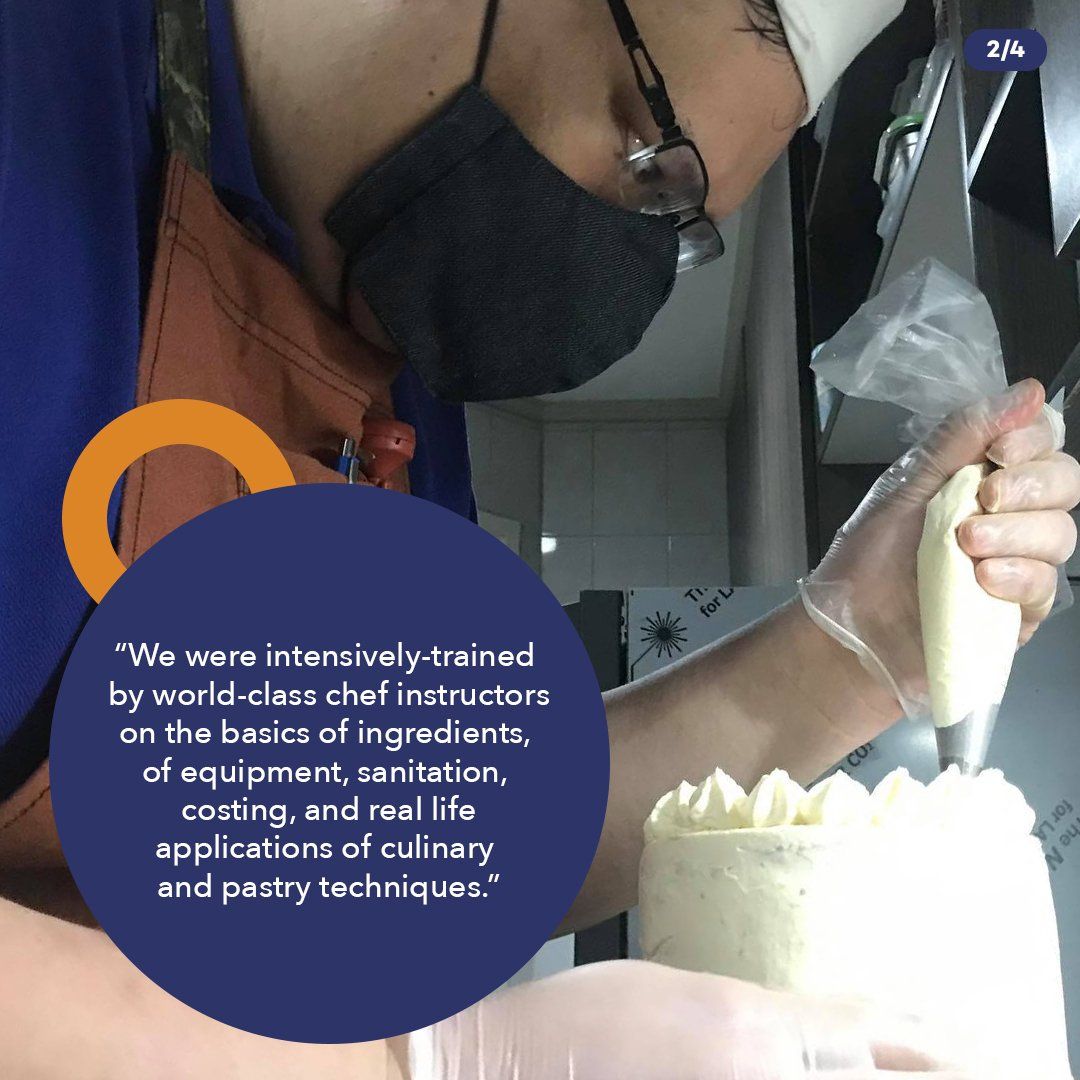 Person piping frosting onto a white cake in a kitchen, wearing black gloves and a black top.