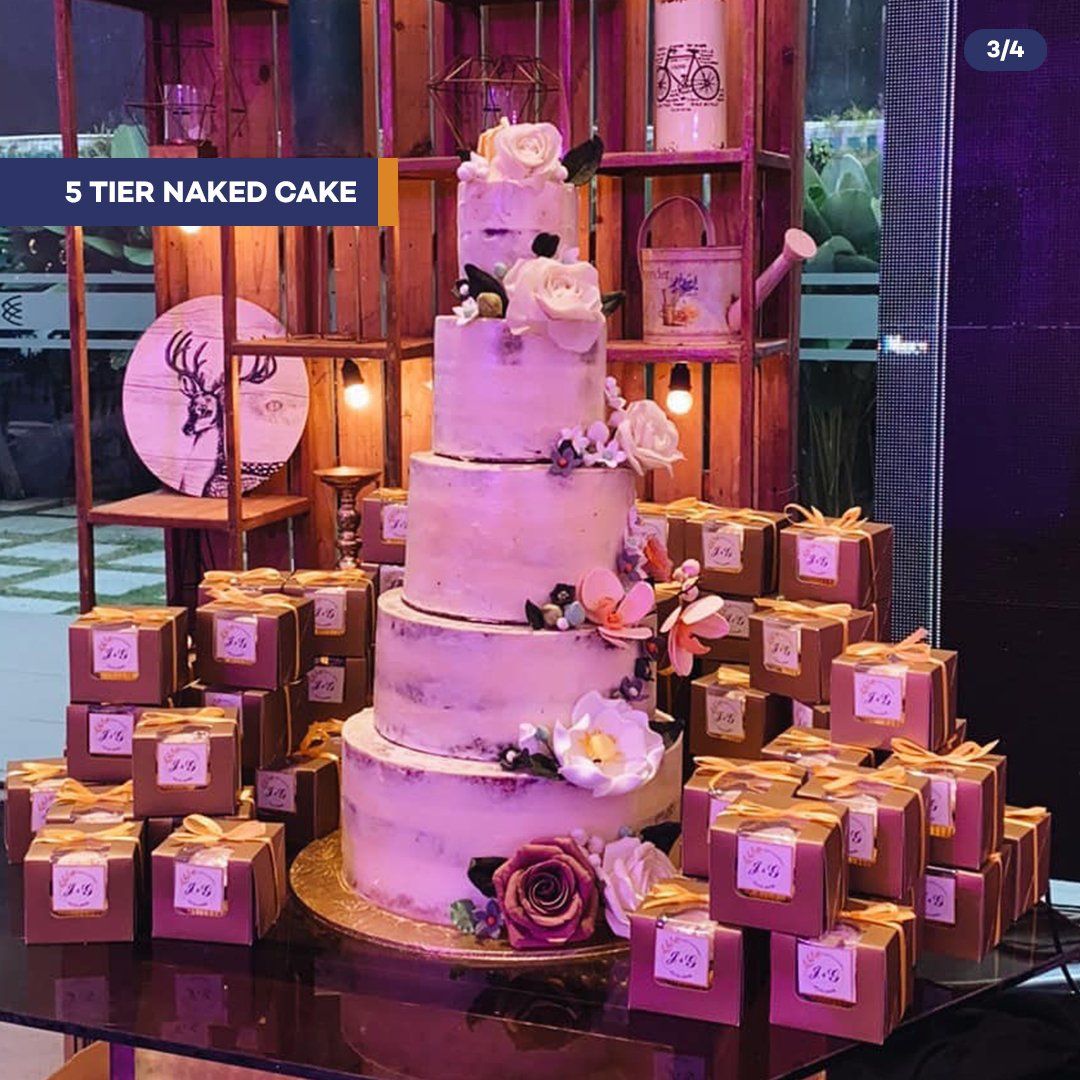 Five-tier white wedding cake with flowers, surrounded by pink gift boxes on a decorated table