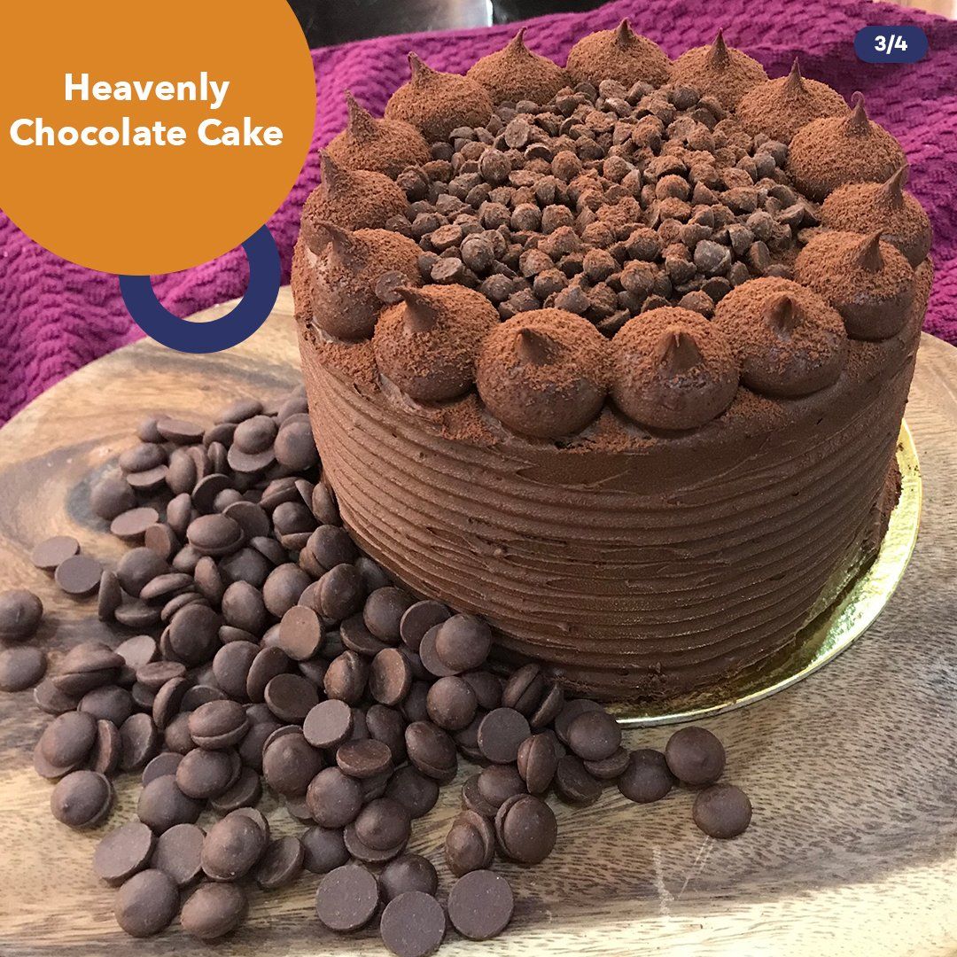 Chocolate cake topped with chocolate pieces, surrounded by chocolate chips on a wooden board.