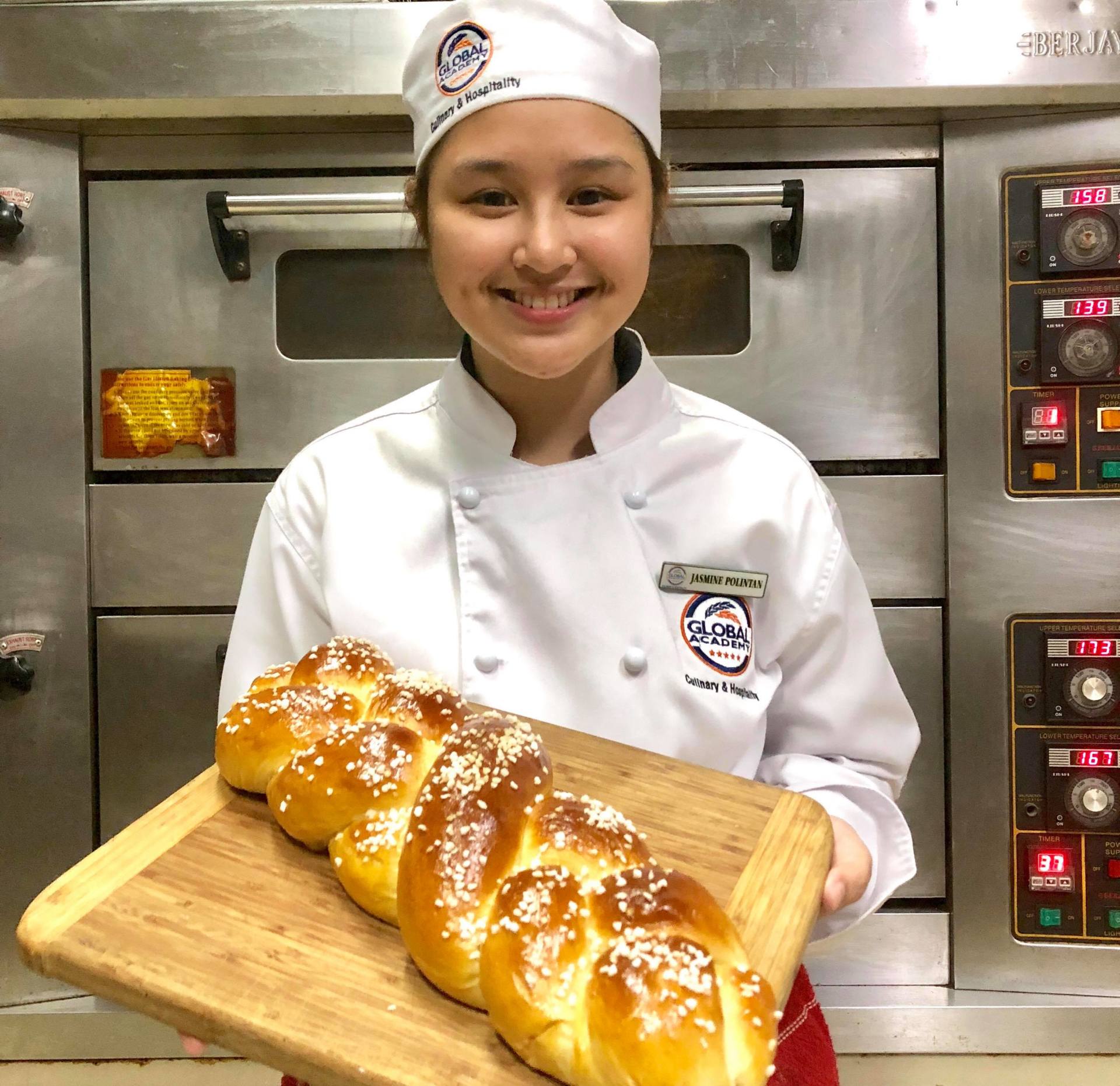 Chef in white uniform holding a tray of freshly baked braided bread in a commercial kitchen