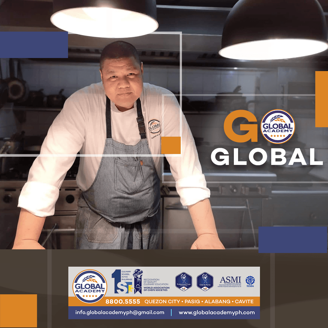 Chef in apron leaning over a counter in a commercial kitchen with “GLOBAL” branding and overhead lights