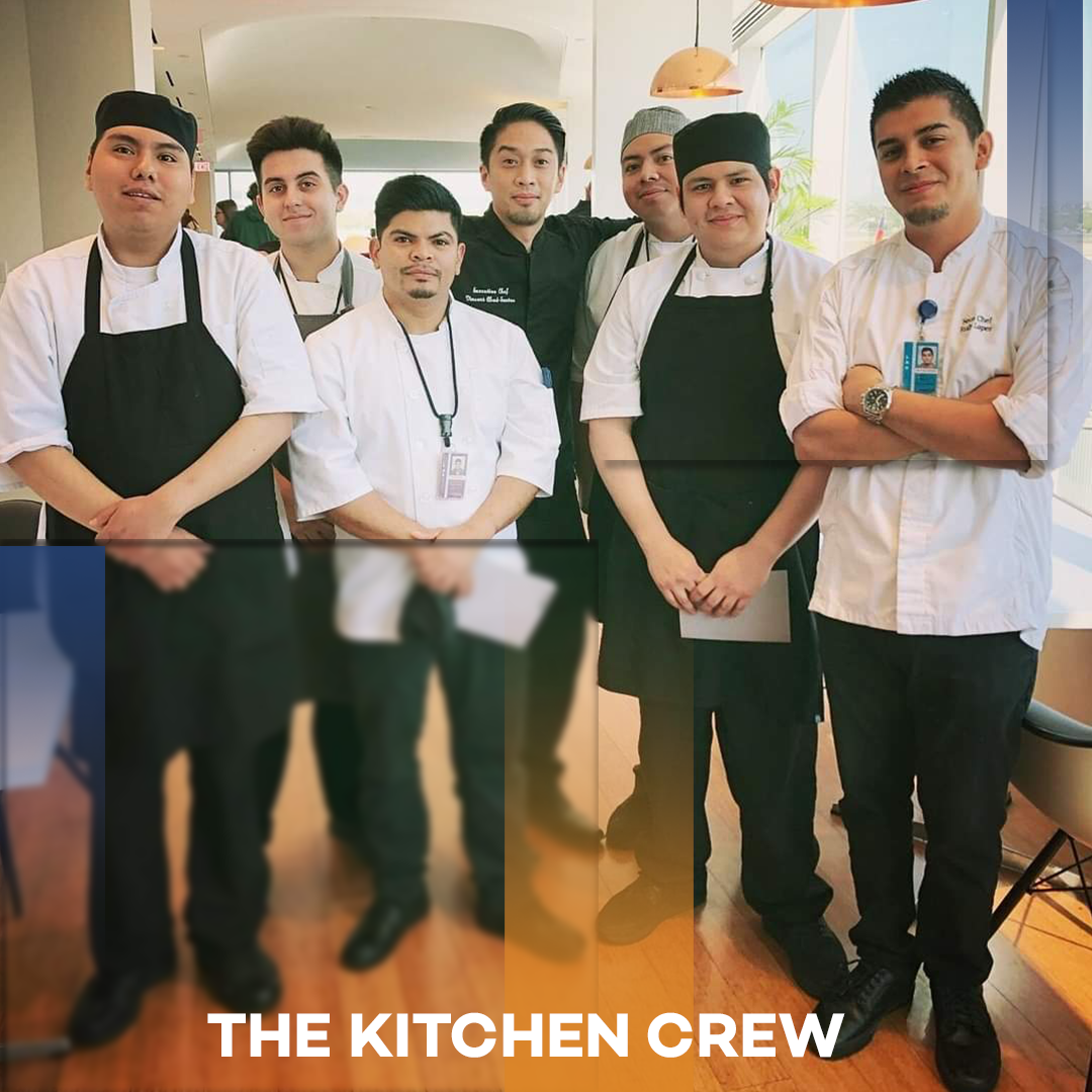 Six kitchen staff in aprons and chef coats standing together in a bright kitchen, labeled “THE KITCHEN CREW”