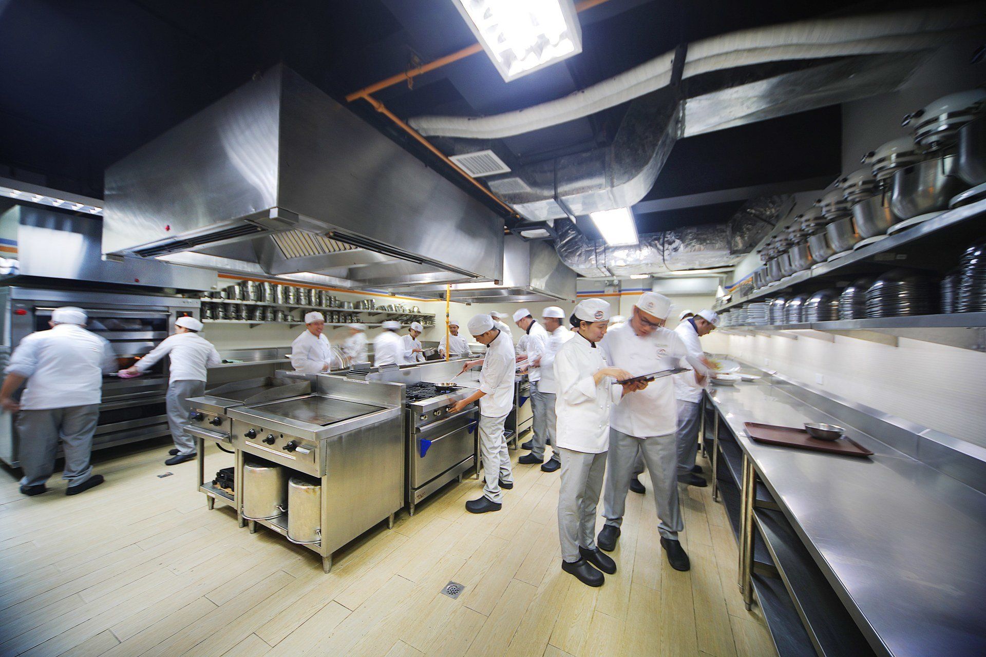Chefs in white uniforms working in a busy commercial kitchen with stainless steel counters and bright overhead lights