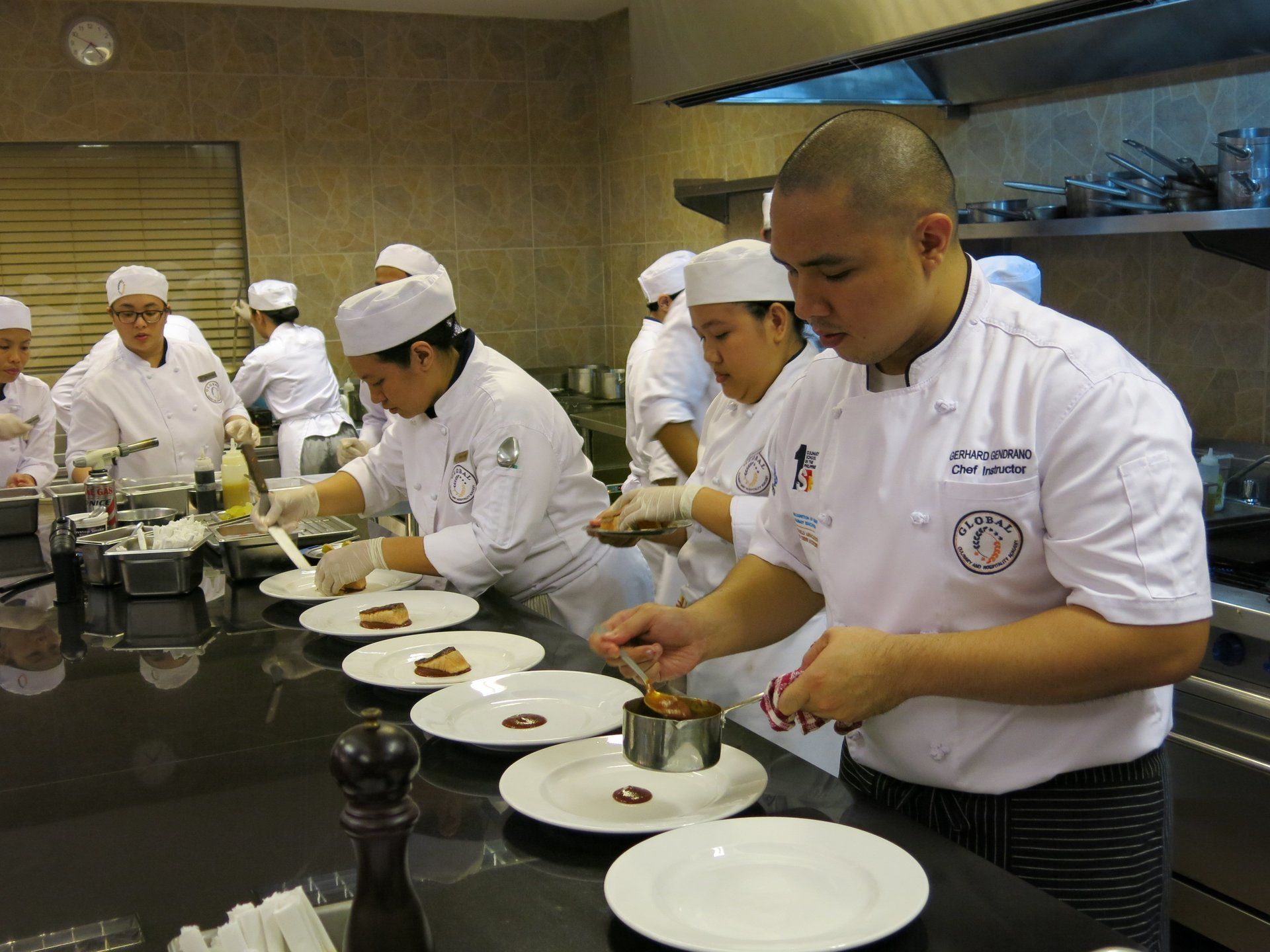 Chefs in white uniforms plating dishes in a professional kitchen during a cooking competition