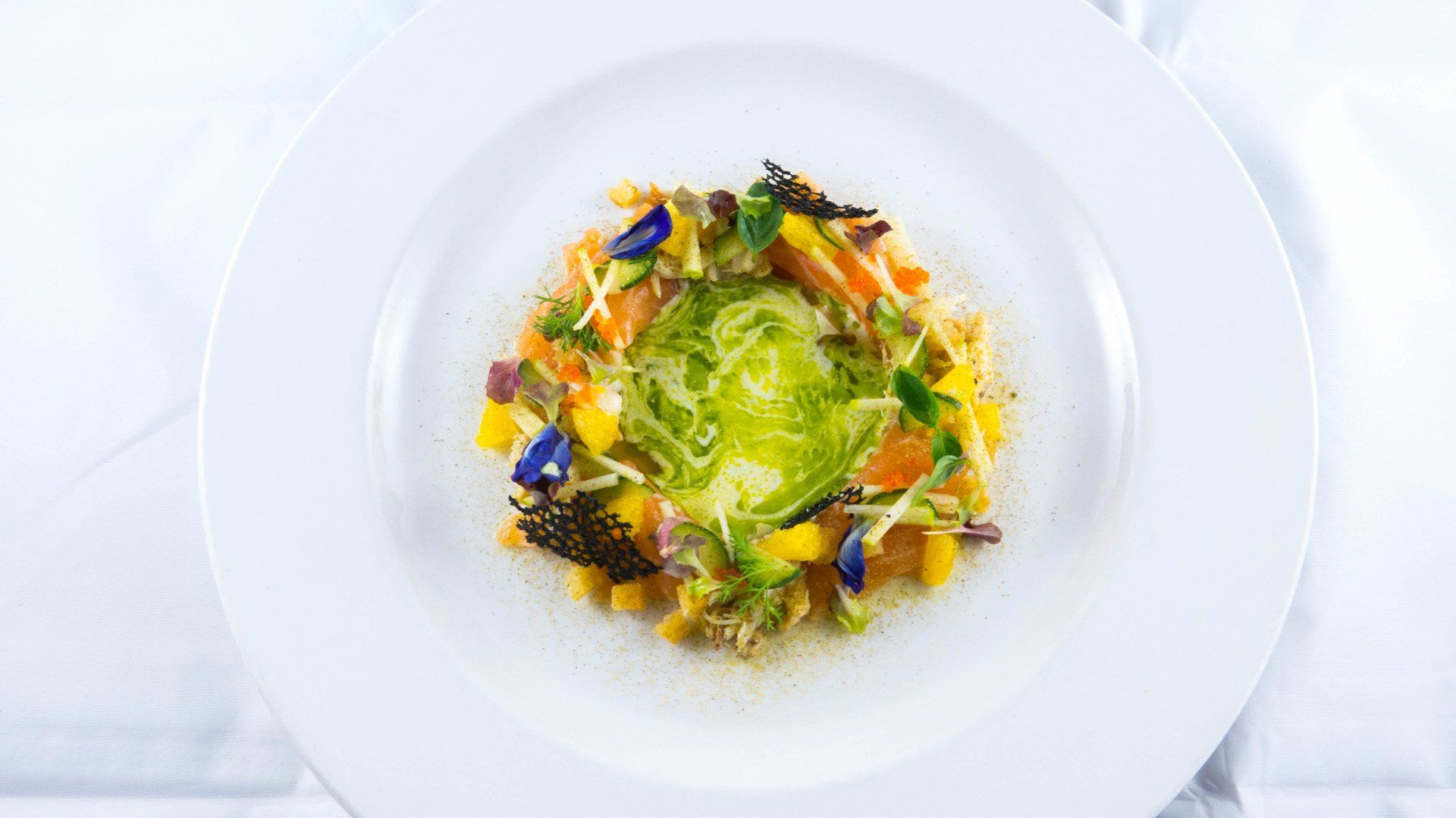 Gourmet plated salad with green center, colorful vegetables, and edible flowers on a white dish