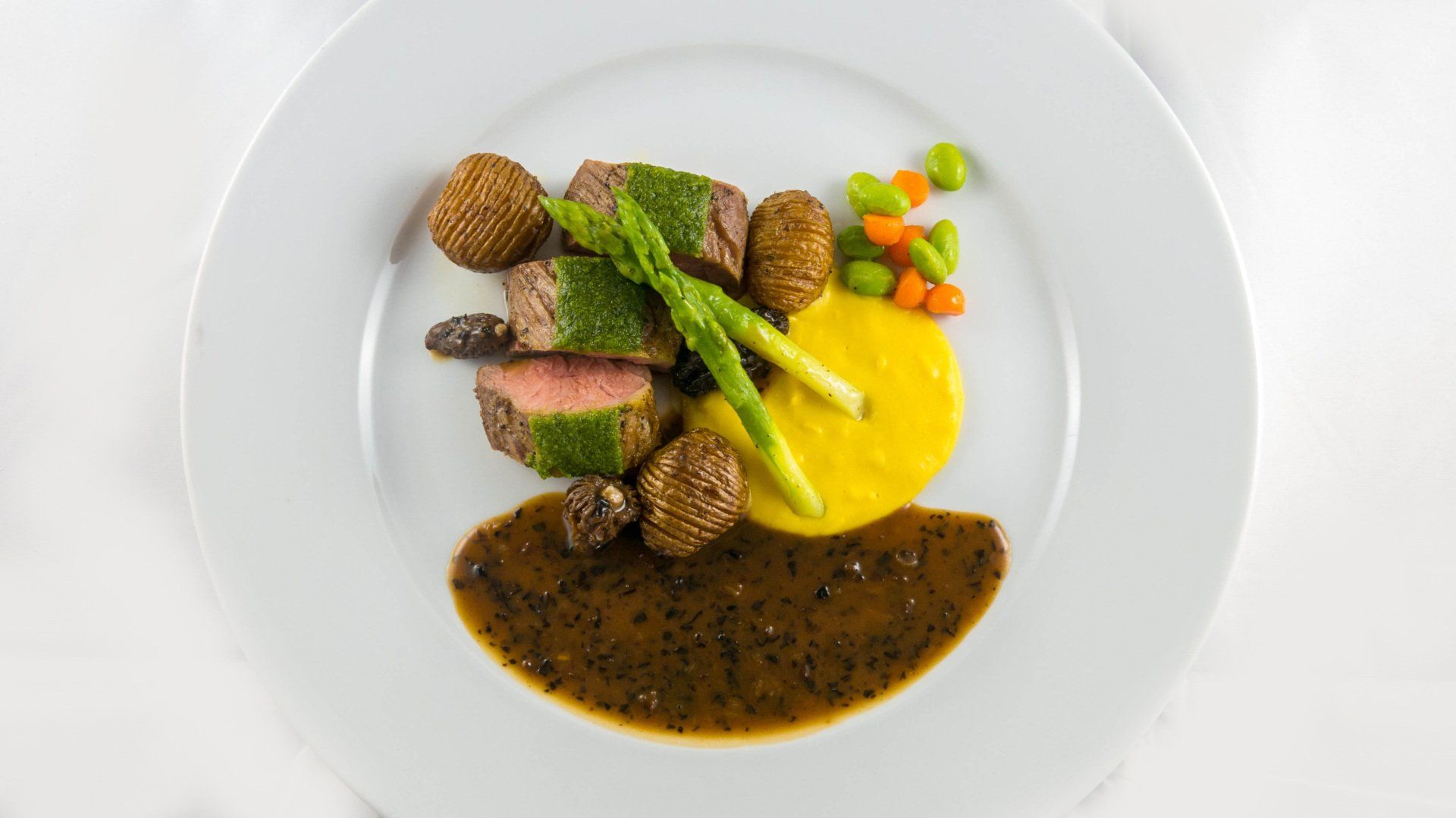 Plated gourmet dish with sliced meat, asparagus, vegetables, and three sauces on a white plate