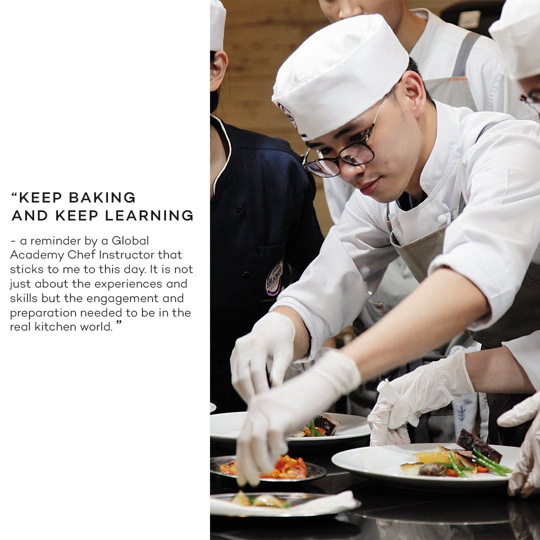 Chef plating food during a cooking class beside a poster that reads “KEEP BAKING AND KEEP LEARNING”