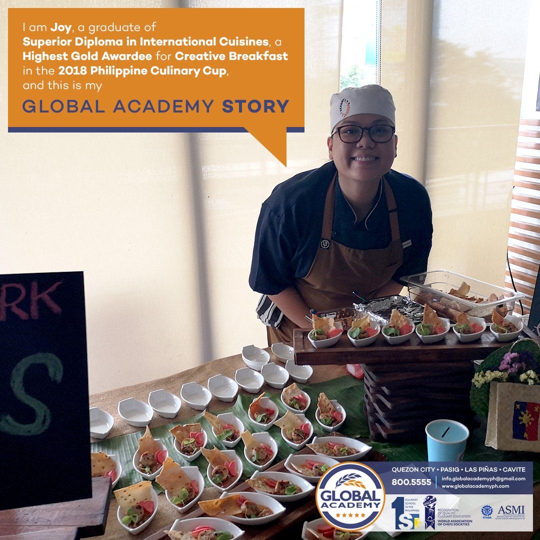 Smiling vendor behind a table of packaged desserts with a “Global Academy Story” sign at an indoor event