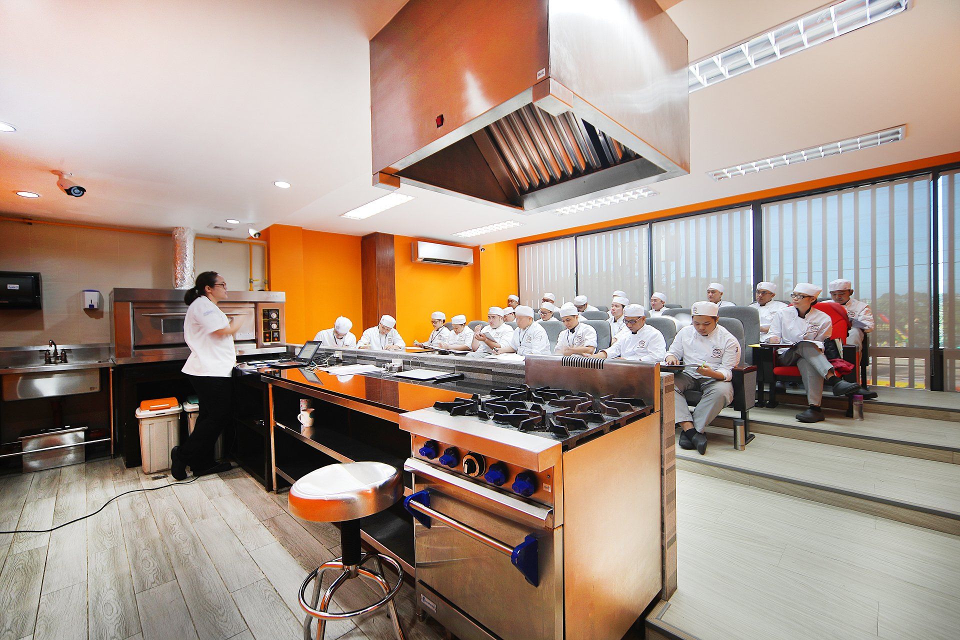 Commercial kitchen with chefs preparing food beside a dining area with seated guests
