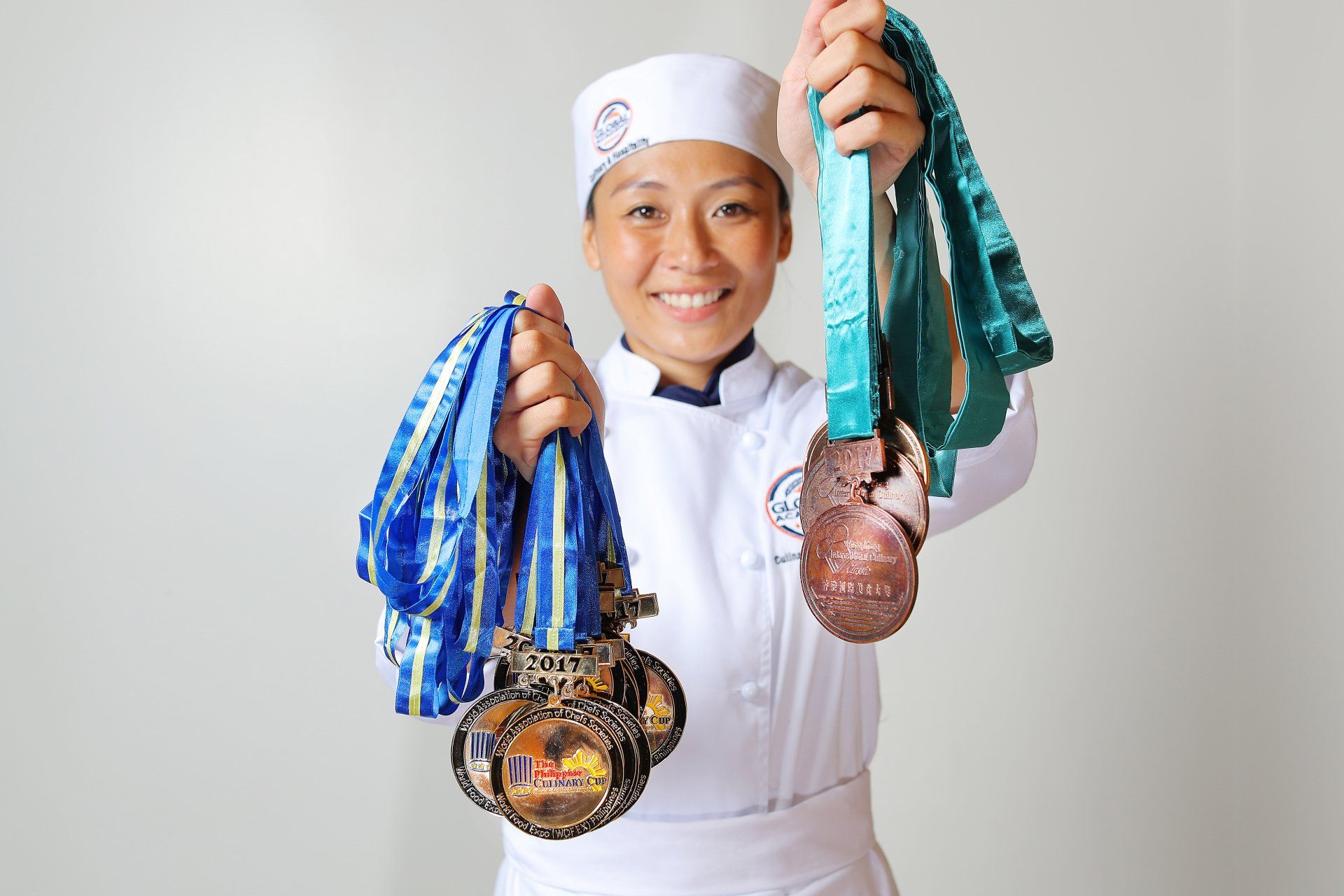 Person in chef uniform holding up two decorated bead necklaces, one blue and one teal.