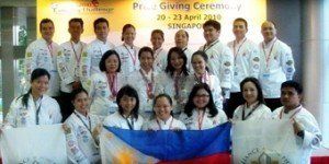 Group of people in white coats posing at a ceremony, holding a large Philippine flag and a sign.