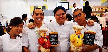 Four people in white shirts smiling and holding packaged products at an indoor event booth