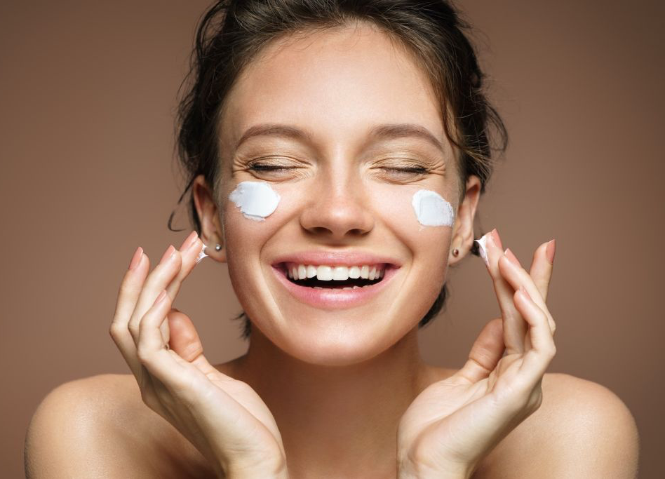 Uma mulher está sorrindo enquanto aplica creme no rosto.
