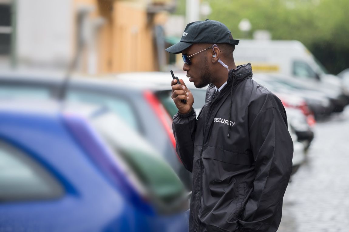 Man in black jacket and cap using a phone beside parked cars on a wet street
