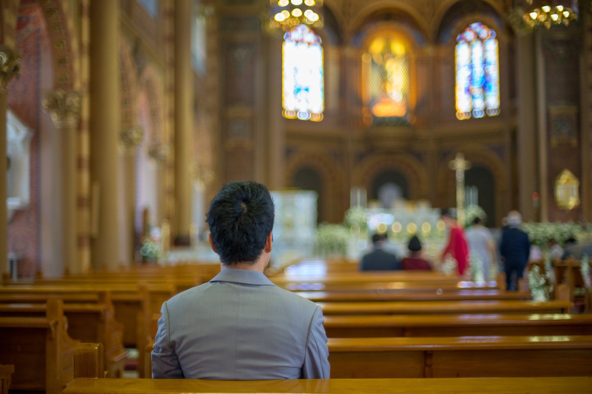 Person seated in a church pew, facing the altar with blurred figures in the background.