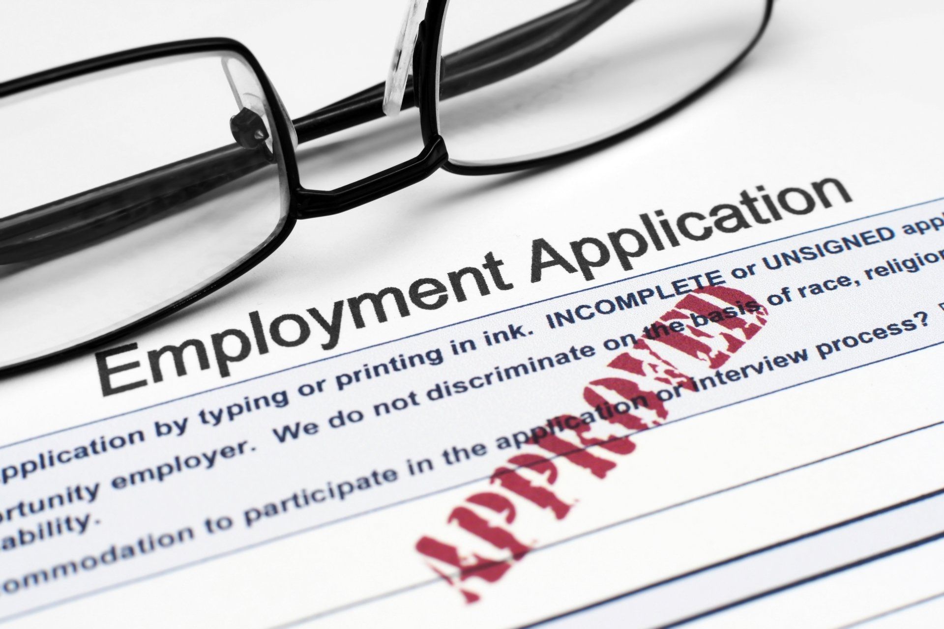 Employment application form with glasses and red “Approved” stamp