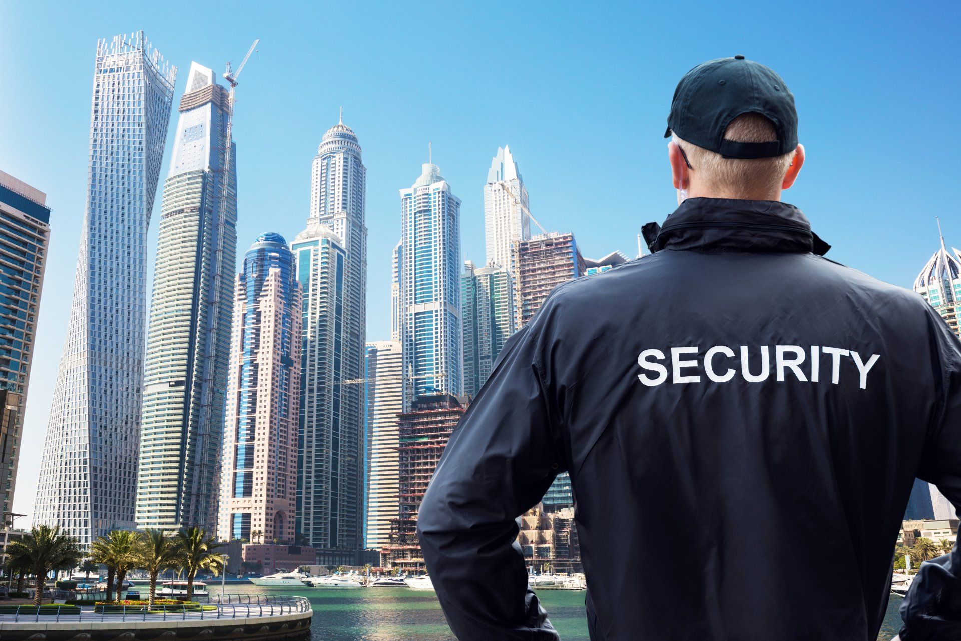 Security guard facing modern skyscrapers by the waterfront under a clear blue sky