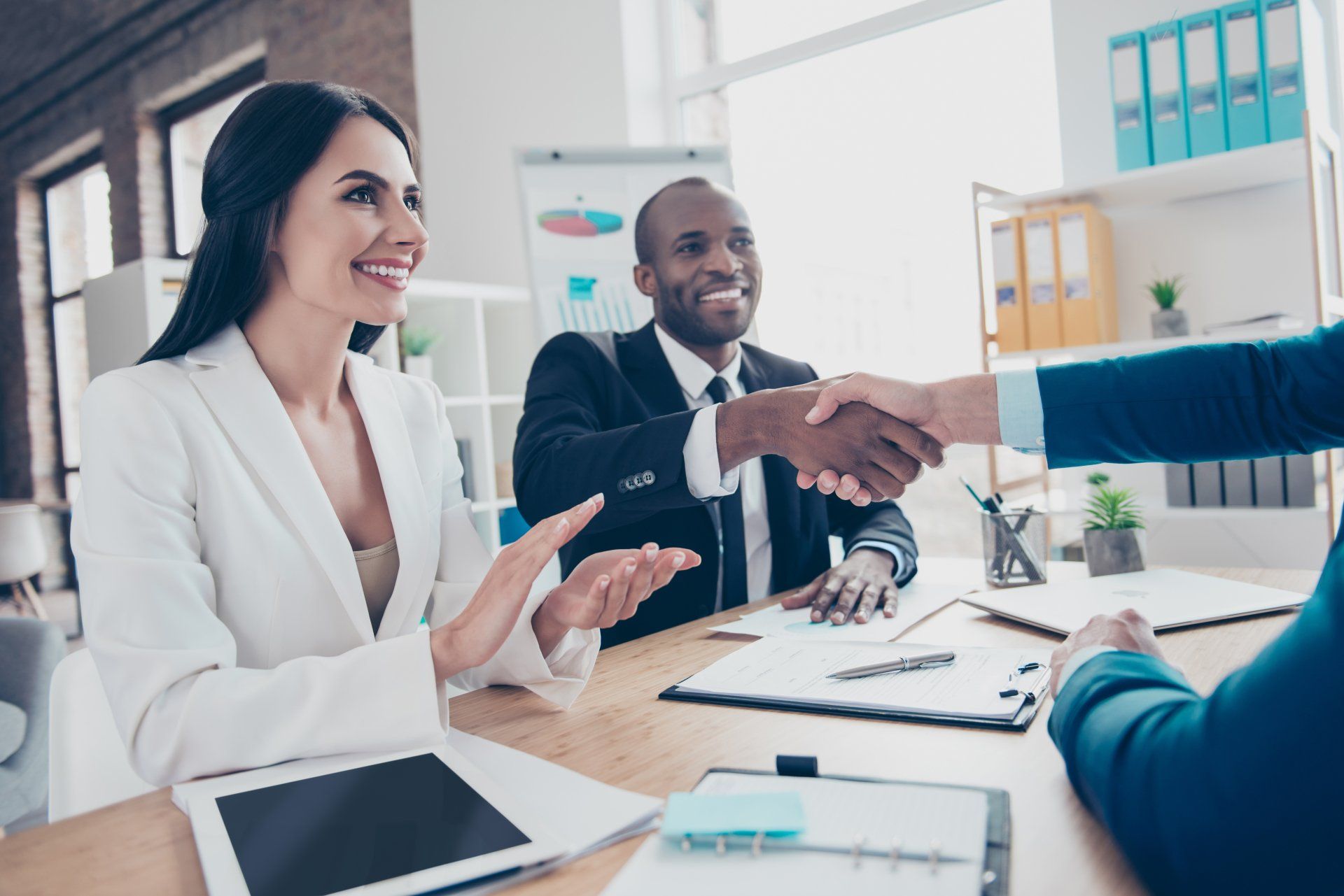 Business meeting with two people shaking hands across a conference table in a bright office
