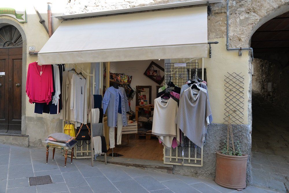 Negozio di abbigliamento con capi esposti all'esterno sotto una tenda da sole su una strada lastricata.